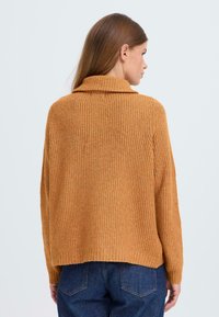 Rostfärgad stickad tröja med ribbad textur, med en vid krage och avslappnad passform, parat med blåjeans.
