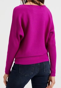 Fuchsia-ribbad tröja med avslappnad passform, bred halsringning och långa ärmar; kombinerad med mörkblå jeans som visar en slät yta.