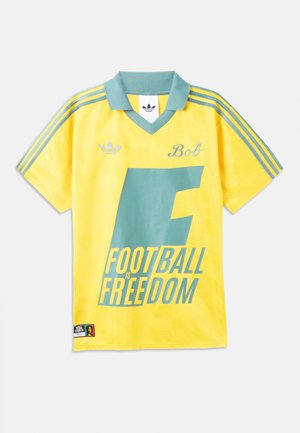 Κίτρινη φανέλα ποδοσφαίρου Adidas με τιρκουάζ γιακά και ρίγες, μεγάλος κείμενος „F Football is Freedom“ και το όνομα "Bob" κεντημένο στο στήθος.