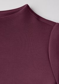 Camicia bordeaux a maniche corte con colletto alto, realizzata in un tessuto liscio e elastico con una finitura pulita e una leggera texture.