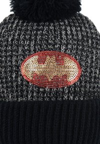 Gorro de punto negro y gris con un pompón, que presenta un logotipo de Batman en lentejuelas doradas y rojas sobre un parche ovalado liso.