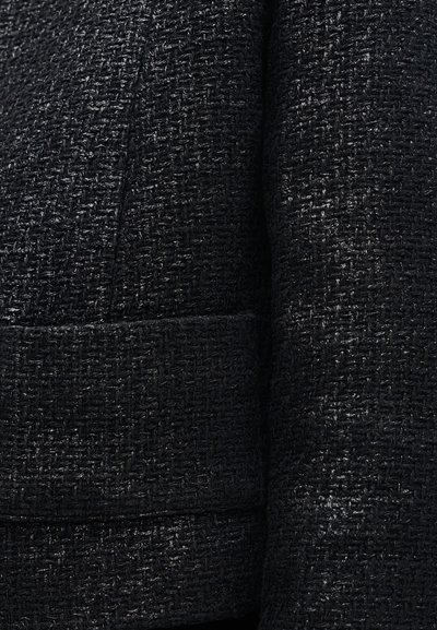 Detailný záber na čiernu tkanú textúrovanú látku na odev s vreckom a švovými detailmi.