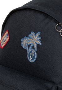 Mochila de tela negra con un parche rojo de "MOTEL Vacation" y palmeras bordadas en azul con un logo "EP". Incluye un anillo de metal.