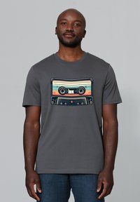 Graues T-Shirt mit einem bunten, retro Kassettenmotiv auf der Vorderseite. Kurze Ärmel, Rundhalsausschnitt und weiche Stofftextur.