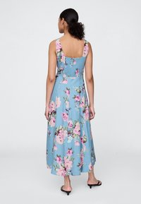 Lys blå maxikjole med blomstermønster i rosa og grønt, ermeløs design og rynket rygg. Glatt stoff med en flytende silhuett.