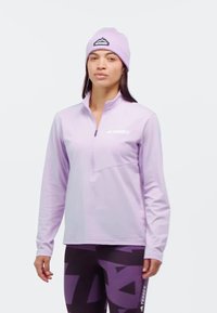 Ljuslila långärmad tröja med halvmatchning, med en bröstficka och vit logotyp. Matchas med mörka mönstrade leggings och en matchande mössa.