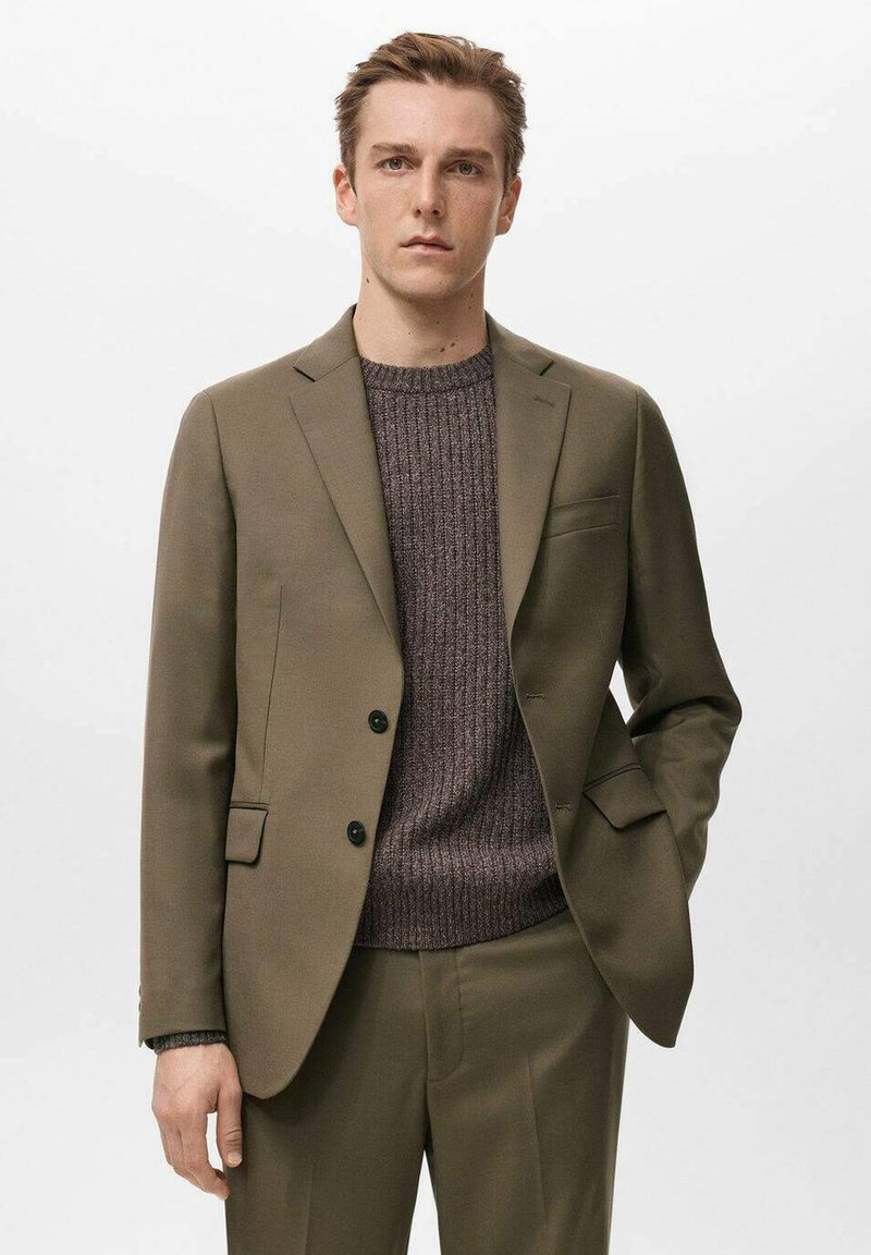 Maslinasto zeleni sako s reverima s usjekom i dva crna gumba, uparen s teksturiranim smeđim džemperom, koji ima uski kroj i glatki materijal.