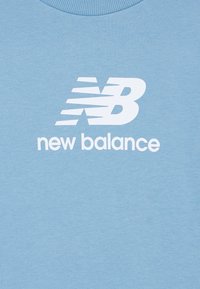 Jasnoniebieska bluza wykonana z miękkiego materiału, ozdobiona dużym białym logo "New Balance" oraz okrągłym dekoltem z prążkowanym wykończeniem.