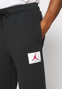 Schwarze Jogginghose aus weichem Stoff, mit einem weißen Aufnäher mit rotem Jordan-Logo auf der linken Tasche und einem elastischen Bund.