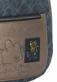 Gepolsterte navyfarbene Stofftasche mit braunem Kunstlederpaneel, ausgestattet mit einer goldenen Katzenbrosche und einem dekorativen Druck von Taschen und Texten in unterschiedlichen Schriftarten.