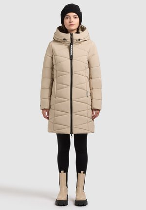 Bežna puhovka z zadrgo spredaj, kapuco in geometrijskim prešitjem. Nošena čez črne legice in bež gležnjarje z črnimi podplati.