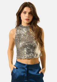 Crop top en sequins argentés avec un col haut, design ajusté et texture scintillante. Associé à un pantalon satin bleu taille haute.