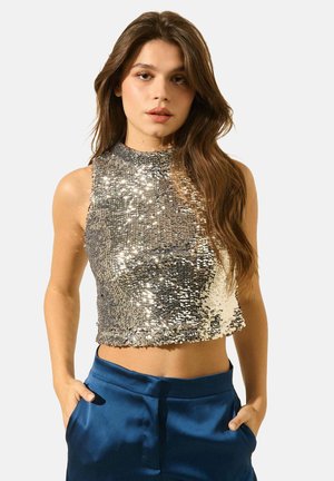 Crop top en sequins argentés avec un col haut, design ajusté et texture scintillante. Associé à un pantalon satin bleu taille haute.