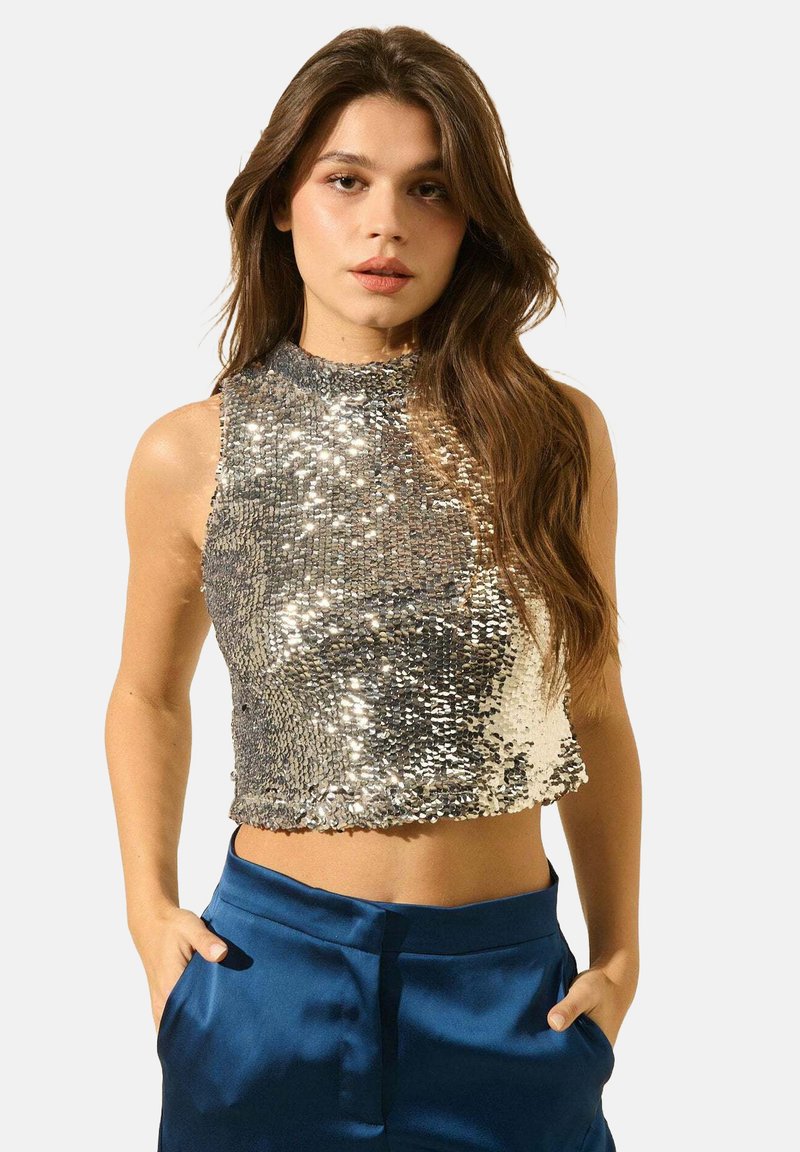Crop top en sequins argentés avec un col haut, design ajusté et texture scintillante. Associé à un pantalon satin bleu taille haute.