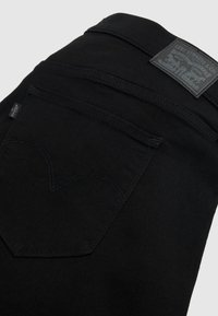 Μαύρα τζιν Levi's διπλωμένα, με εμφανή την πίσω τσέπη που φέρει την ετικέτα με το λογότυπο Levi's και το δερμάτινο έμβλημα της μάρκας στη μέση της ζώνης.