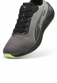 Juoda ir pilka sportinė avalynė su tinklelio raštu, raišteliais ir neoninėmis žaliai padais. Yra paminkštinta apykaklė ir kvėpuojanti viršutinė medžiaga.