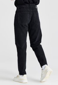 Pantalones de mezclilla negra con perneras ajustadas, que presentan una cintura alta, dos bolsillos traseros y una superficie texturizada. Combinados con zapatillas blancas.