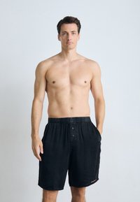 Black cotton shorts with an elastic waistband and button closure, featuring side pockets and a soft texture.