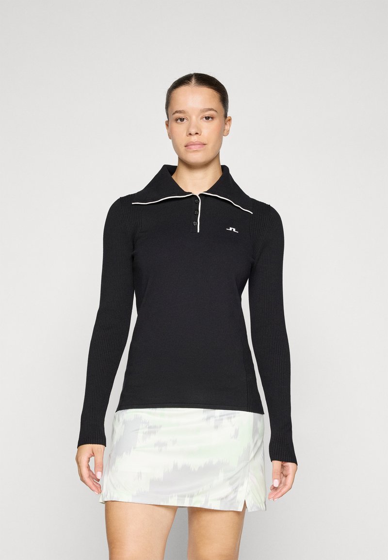 Black long-sleeve polo shirt with ribbed texture, white piping along collar, and a three-button placket. Worn with a light patterned skirt.