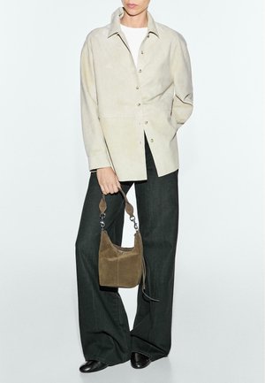 Beige suedine overhemd met knopen, donkere, wijde pantalon, en een kleine bruine suedine tas met zilverkleurige accenten. Zwarte schoenen maken de look compleet.