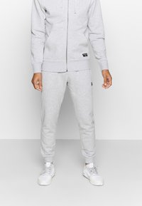 Grauer Baumwollzipper mit Fronttaschen und gerippten Bündchen, kombiniert mit passenden grauen Jogginghosen. Weiße Sneaker runden das Outfit ab.