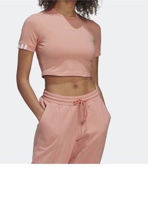 Vaaleanpunainen lyhythihainen cropped-toppi, jossa on kultainen logo rinnassa, yhdistettynä samansävyisiin vaaleanpunaisiin collegehousuihin, joissa on elastinen vyötärö ja taskut.