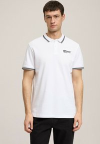 Biała koszulka polo z dwoma guzikami, czarno-białym kołnierzykiem i mankietami, z logo na lewym piersi.