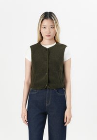 Olivenfarge fleecevest med rund hals, frontknapper og kontrastbesetning, båret over en hvit skjorte og paret med mørke jeans.