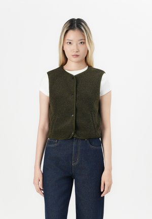 Olivengroen fleece vest met een ronde halslijn, voor knopen en contrasterende afwerking, gedragen over een wit shirt en gecombineerd met donkere spijkerbroek.