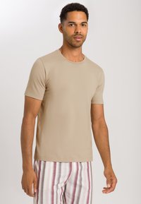 Beige tričko s krátkým rukávem vyrobené z měkké tkaniny, s kulatým výstřihem, spárované s pruhovanými pyžamovými kalhotami v růžových a bílých odstínech.