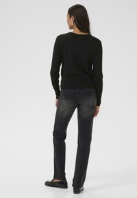 Zwarte trui met een ronde hals, gecombineerd met donkere, licht vervaagde jeans en zwarte instappers; gladde textuur, casual pasvorm.