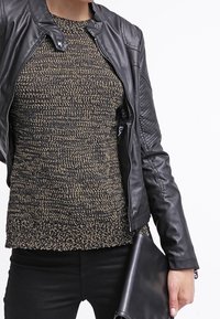 Svart läderjacka med tryckknäppning, strukturerad mörkstickad tröja i beige och brunt, kombinerad med en stilren svart kuvertväska.