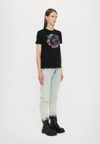 Svart bomull T-skjorte med blomster- og sommerfugl grafisk design på forsiden, kombinert med lyseblå denimjeans og svarte militærstøvler.