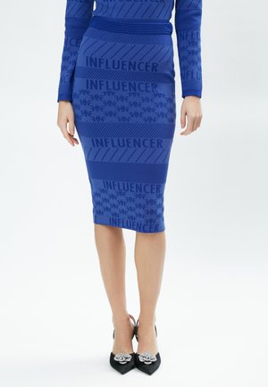 Blauwe kokerrok met een gestructureerd patroon waarop het woord "INFLUENCER" staat, gecombineerd met zwarte puntige hakken met decoratieve accenten.