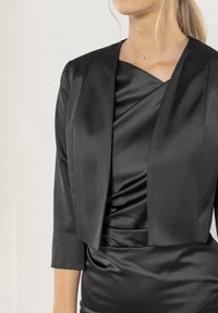 Svart satinjacka med kort design, trekvartsärmar och draperad bodice-detalj. Slät textur, minimalistisk stil, elegant silhuett.