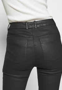 Hoge taille zwarte nep leren broek met een gladde textuur, voorzien van twee achterzakken en riemlussen. Strakke pasvorm.