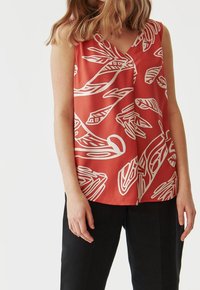 Blusa senza maniche di colore corallo realizzata in tessuto leggero, con motivi bianchi a foglia e vortice. Design a V, vestibilità rilassata e texture liscia.