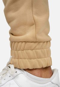 Beige joggingbroek met gather-mouwtjes bij de enkels, gecombineerd met witte sneakers met vetersluiting en een gestructureerde zool.