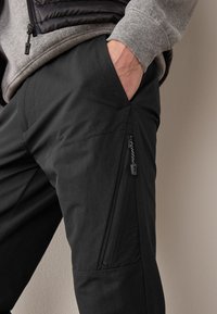 Pantalon d'extérieur noir avec une texture douce, doté de poches latérales et de fermetures éclair pour un rangement sécurisé. Conçu avec des coutures renforcées pour une durabilité accrue.