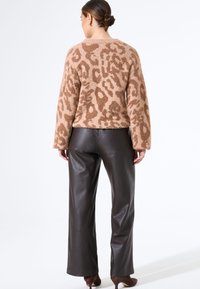 Braun-gefärbter Leopard-Print-Pullover mit einer weichen, strukturierten Oberfläche, kombiniert mit hochsitztenden braunen Lederhosen. Akzentdetails umfassen weite Ärmel.