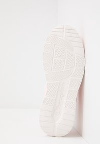 Sneakerin pohja valkoisesta kumista, jossa on tekstuuriset pito-kuviot. Minimalistinen muotoilu, jossa on hienovarainen brändinimi "Champion" kirjoitettuna kursiivilla.