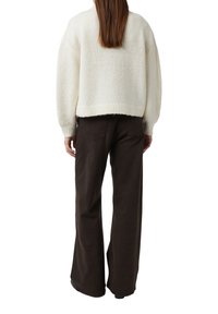 Biały sweter o fakturowanej strukturze z obszernymi rękawami, zestawiony z ciemnobrązowymi, szerokimi spodniami z wysokim stanem. Casualowy, luźny krój.
