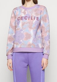 Felpa viola chiaro con un motivo tie-dye in rosa e blu. Presenta la scritta "CECILIE" in lettere texturizzate e luccicanti sul petto.
