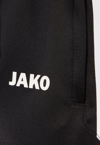 SchwarzeSporthosen aus strukturiertem Stoff mit einem weißen "JAKO"-Logo auf der linken Seite und einem kleinen Taschendetail.