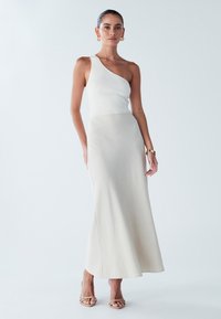 Robe midi à épaules dénudées en maille côtelée couleur crème, avec une jupe fluide et lisse, accompagnée de talons beiges à lanières.