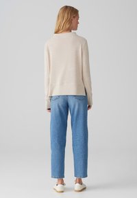 Light beige sweater with a textured finish, featuring a relaxed fit and ribbed hem, paired with high-waisted light blue jeans and white sneakers.