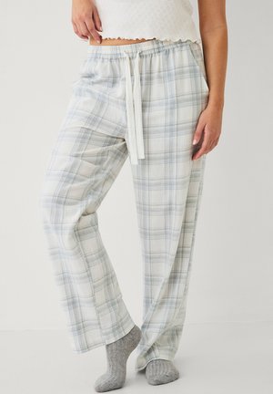Kvinde iført lysegrå og hvide ternede pyjamabukser med snøre i taljen, grå sokker og en hvid ærmeløs top.