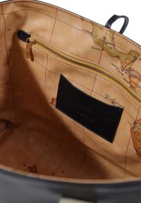 Interno di una borsa nera con una fodera beige decorata con una mappa del mondo, zip dorata e un'etichetta in pelle con testo impresso.