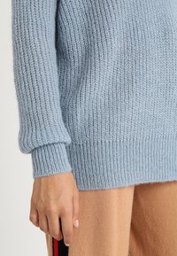 Ljusblå stickad tröja gjord av mjukt garn, har ribbade ärmslut och nederkant, med en avslappnad passform och texturerad yta.