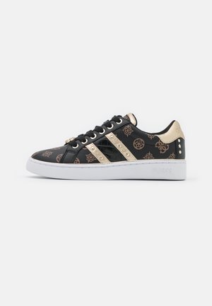 Zapatilla deportiva con estampado en negro y marrón, acentos dorados, cordones negros y suela blanca, mostrando el perfil lateral sobre un fondo blanco.